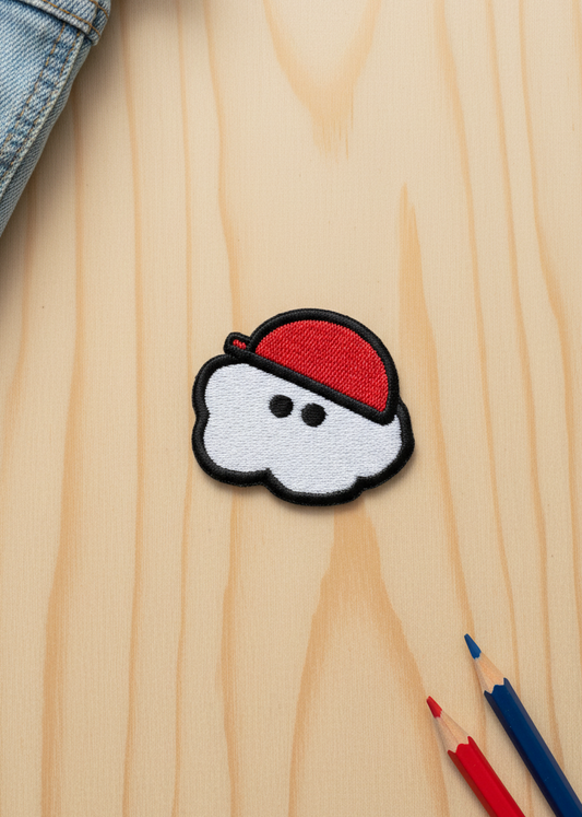 Embroidered patch with a cloud and red hat design on a wooden surface with pencils.