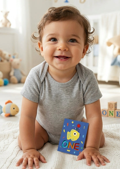 Baby holding a colorful 'ONE' block in a room with toys and 'Happy 1st Birthday' decorations.