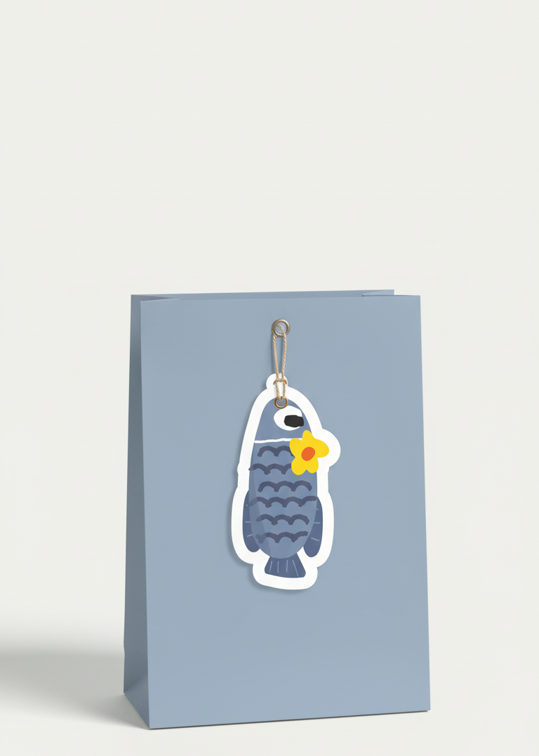 Blue gift bag with a fish with a flower on it's head gift tag on a white surface.